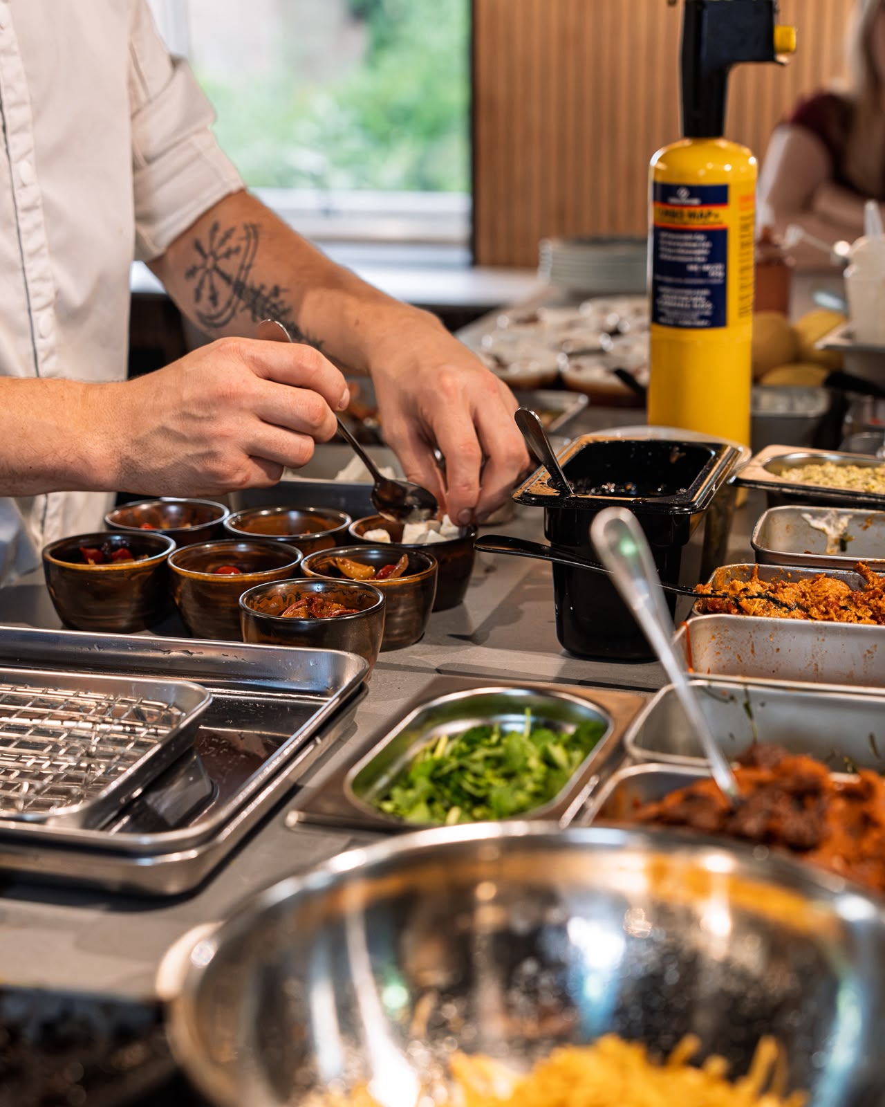 A chef plating small bowls at the Ruger Fjord counter, surrounded by fresh ingredients and preparation trays.